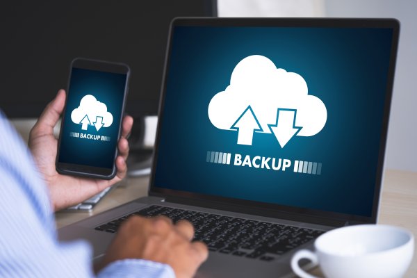 online backup cloud service spideroak one man backing up content on laptop holding smartphone white cup of coffee near laptop