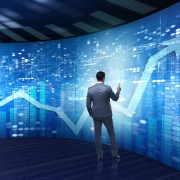 online stock trading man in suit in front of big monitor stocks going up