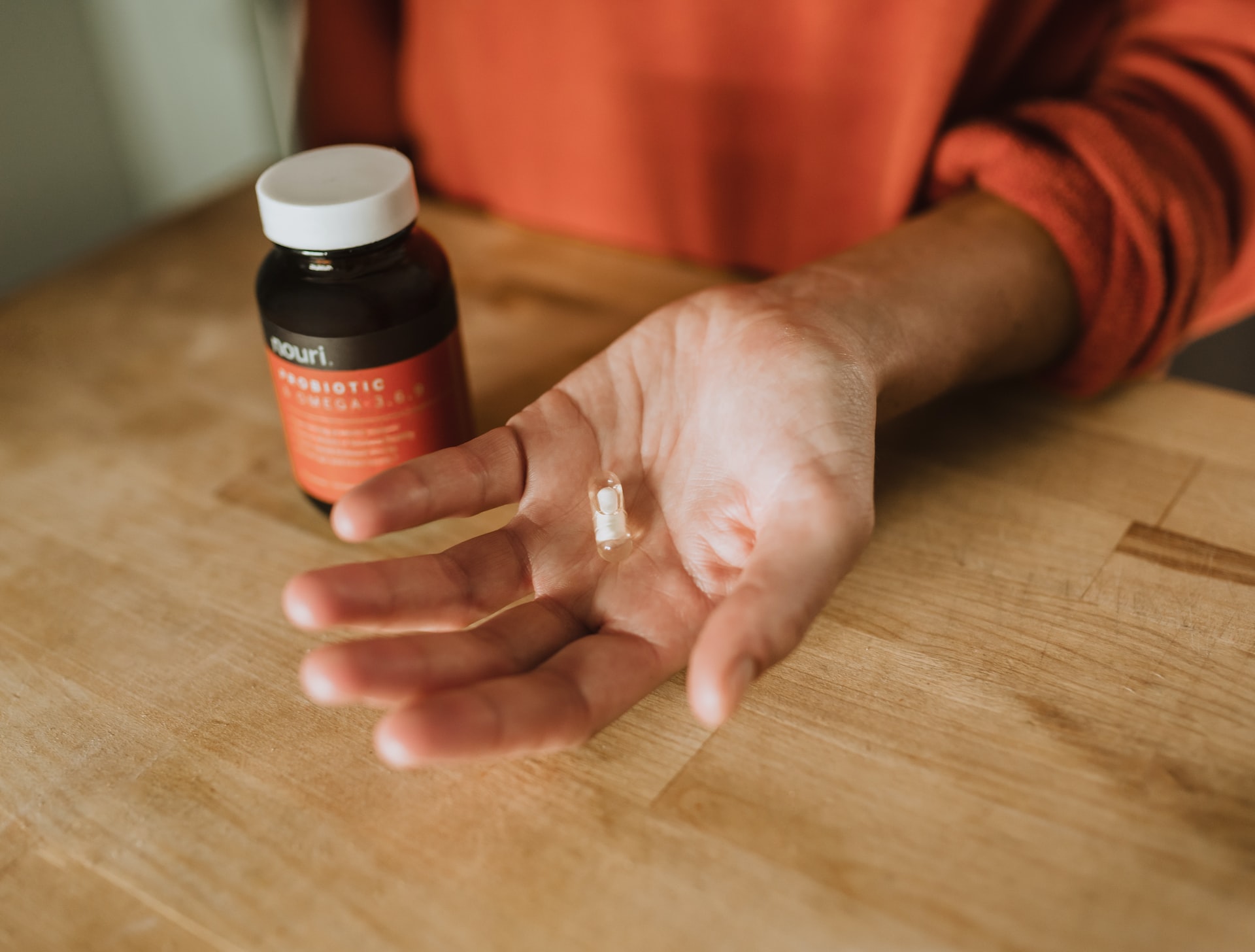 a person with a supplement pill in their hand beside a bottle