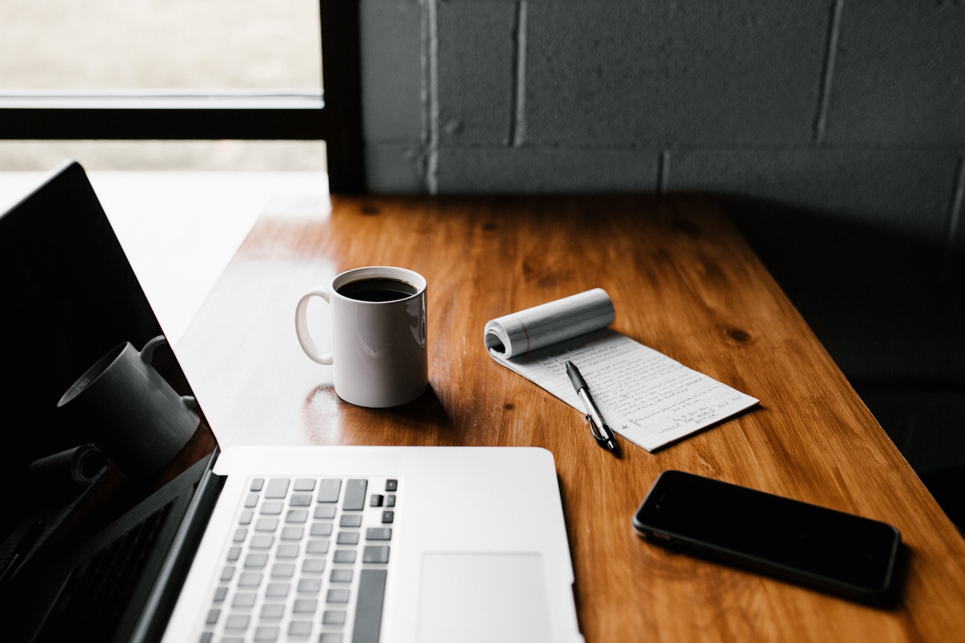 a laptop beside a cup of coffee and notepad