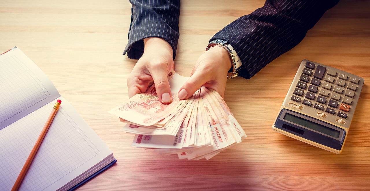 person with cash in their hands beside a book and calculator 