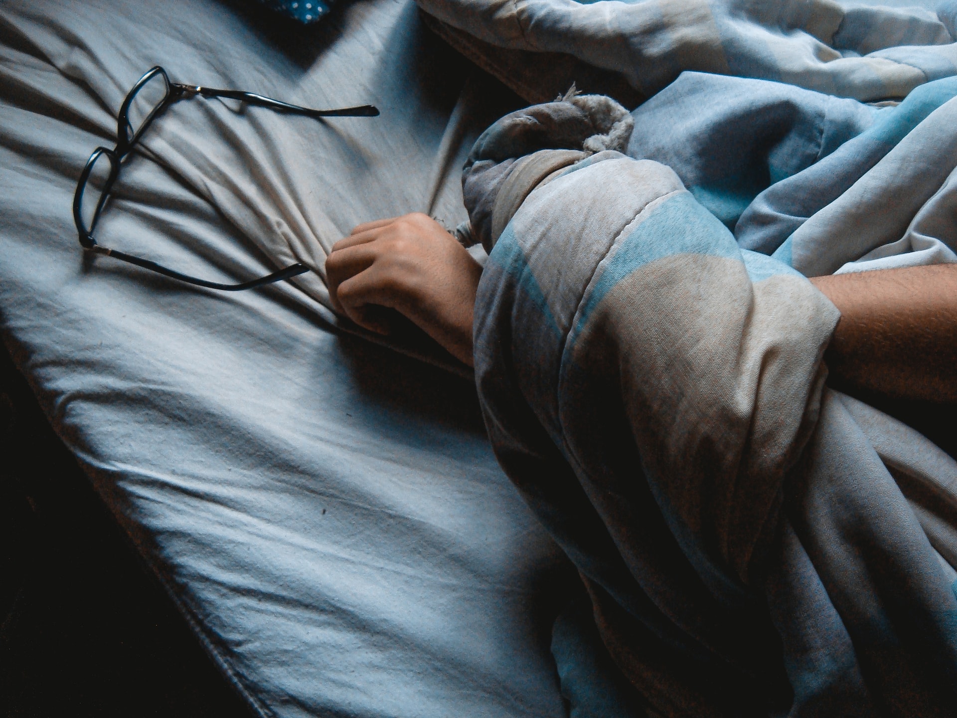 persons arm under a blanket in bed near glasses