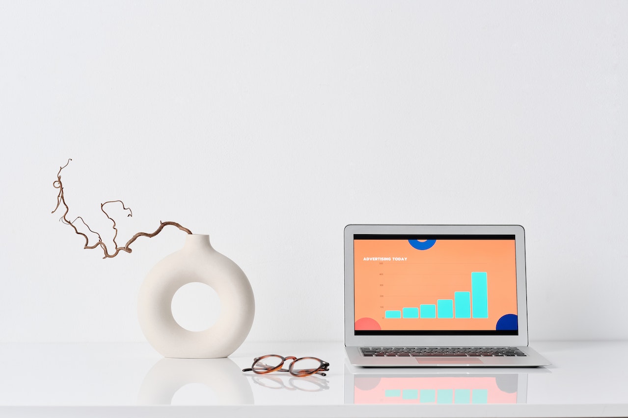 laptop open on a white counter with a white vase beside it