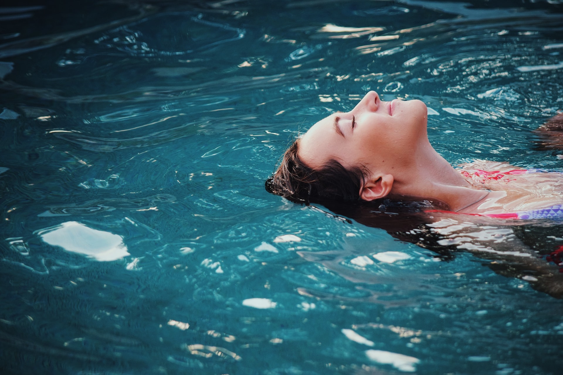 person laying back in a pool in their backyard