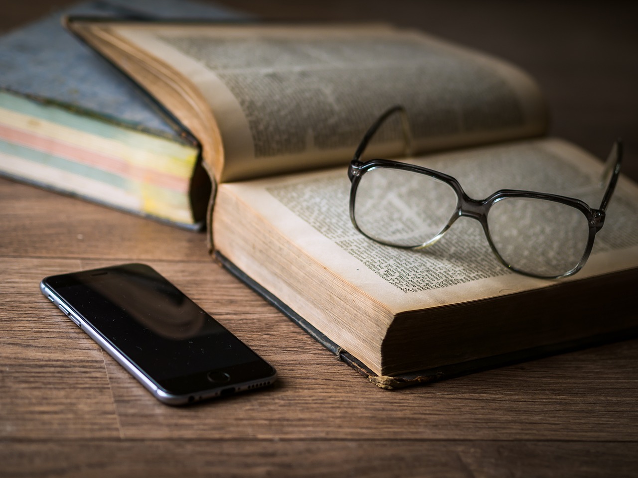 reading glasses on a book, beside a cell phone on a table