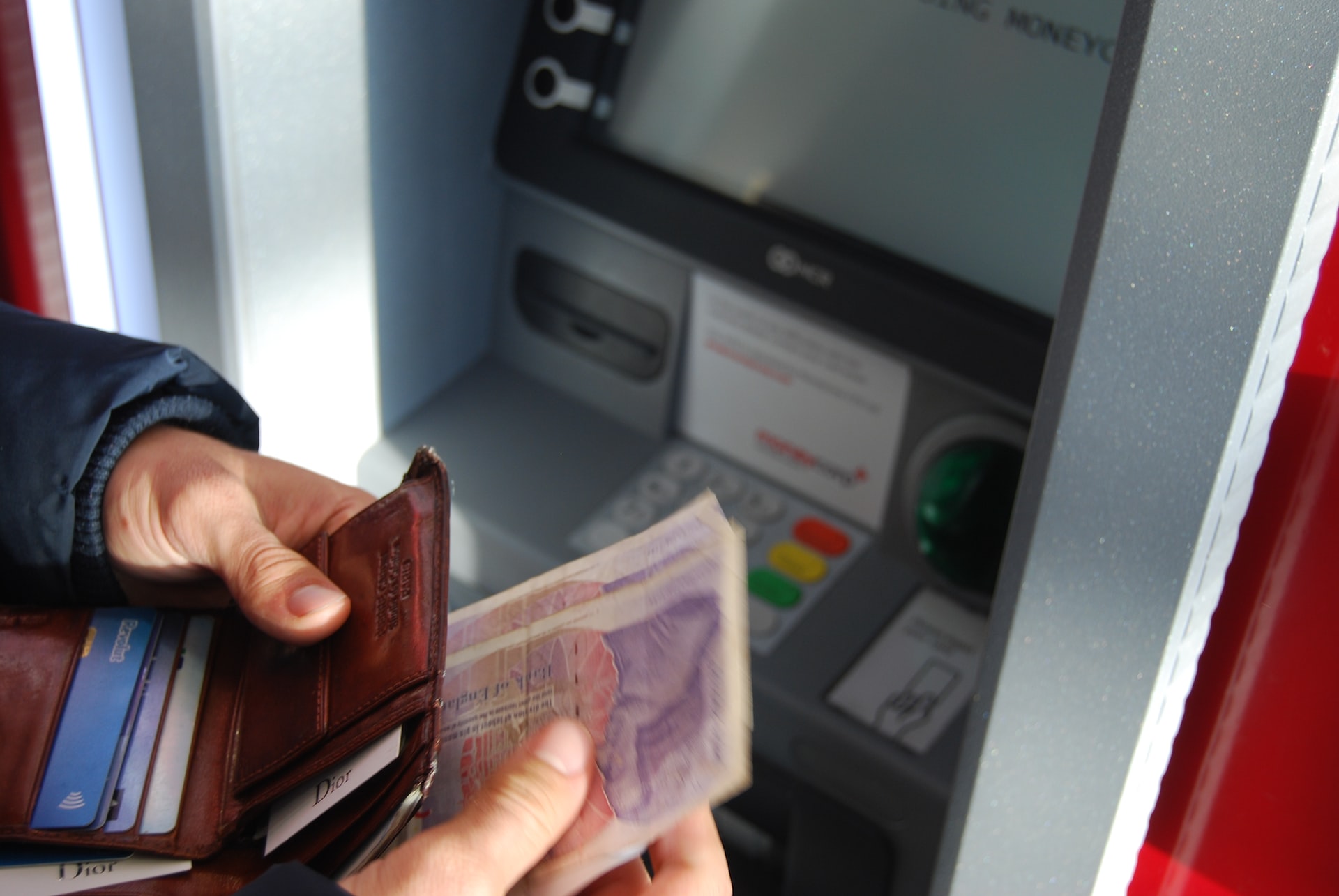 person with cash in their hands by a banking machine