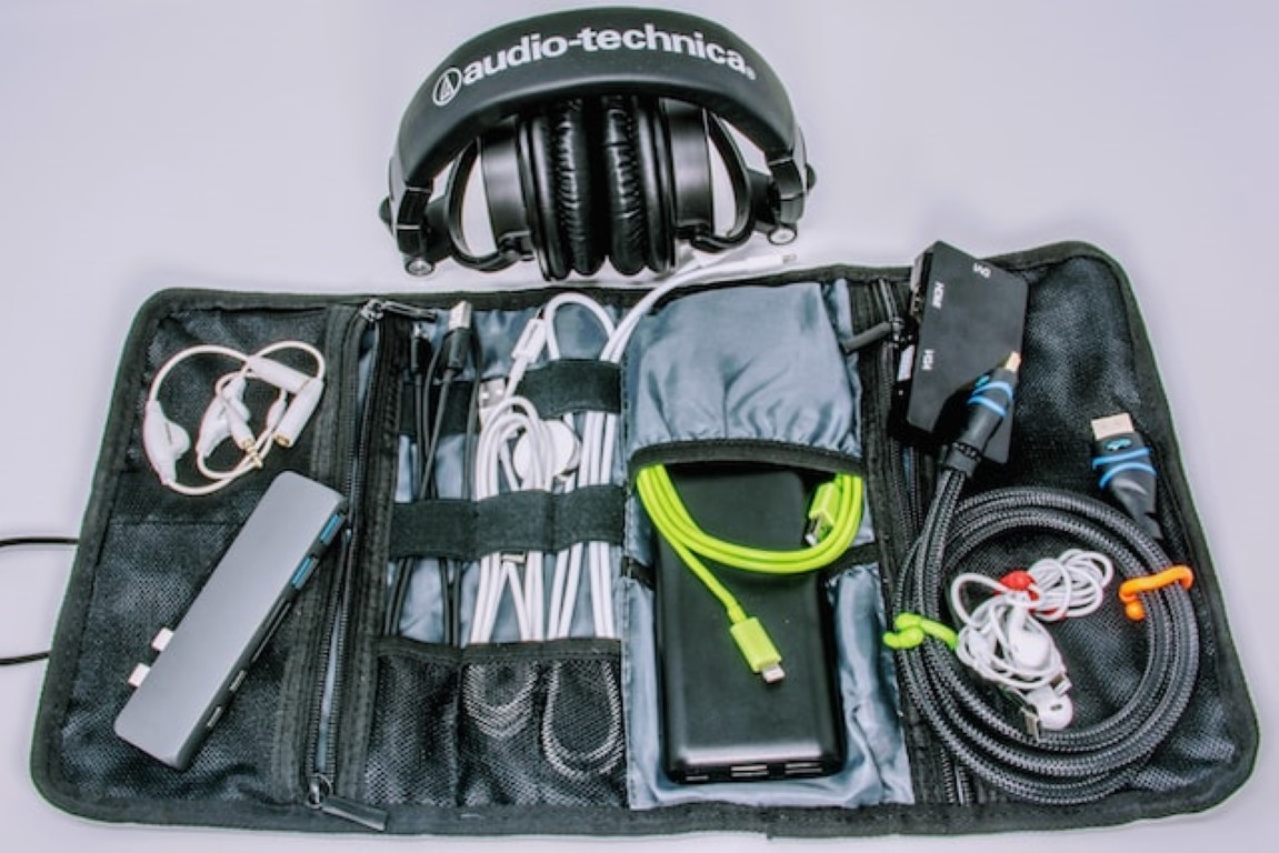 a travel bag open with cables and adapters beside headphones